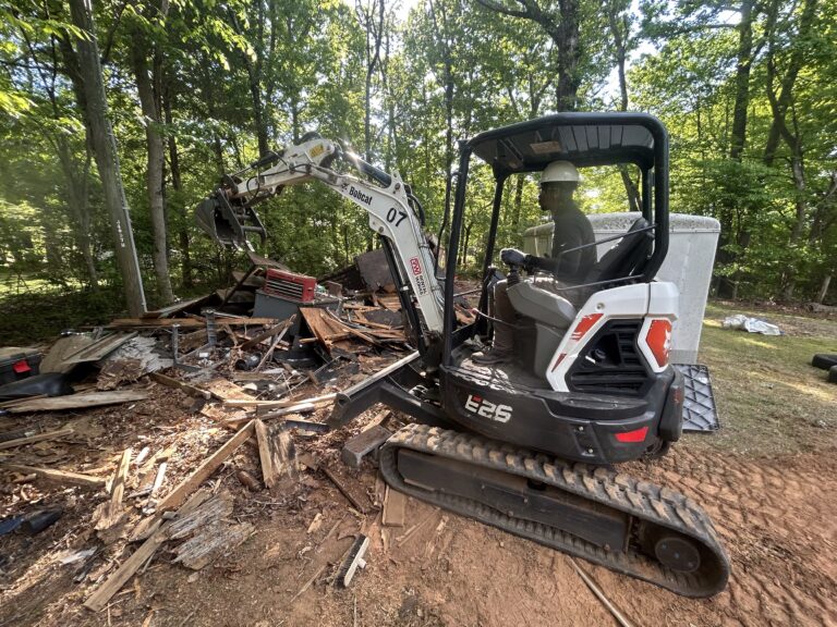 Pro Hauling employee operating an excavator to remove shed debris in Greensboro, NC during a demolition and junk removal project